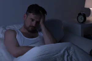 Man sitting awake in bed at night looking stressed, representing poor sleep, insomnia, and the need for sleep-supportive nutrients like zinc