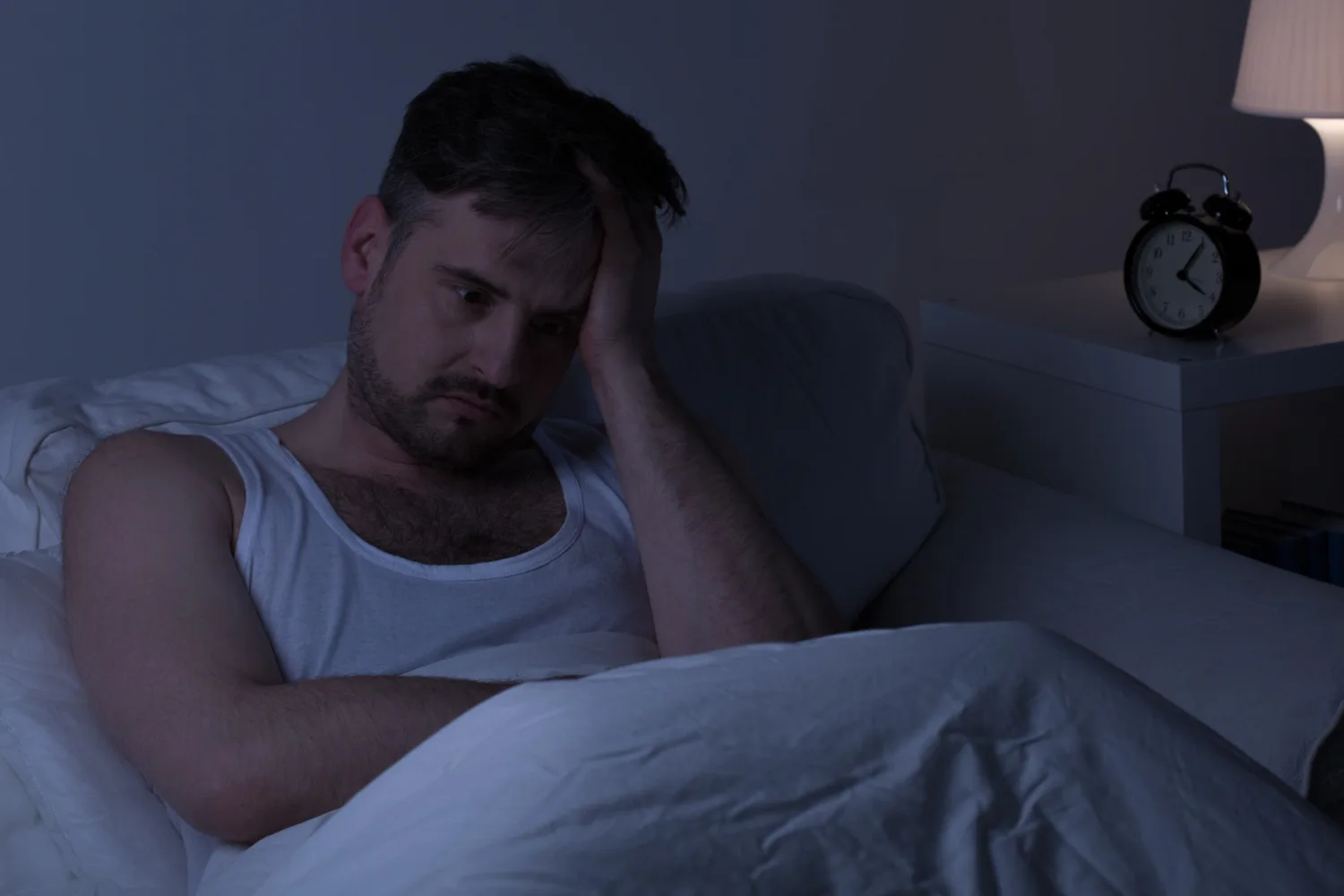 Man sitting awake in bed at night looking stressed, representing poor sleep, insomnia, and the need for sleep-supportive nutrients like zinc