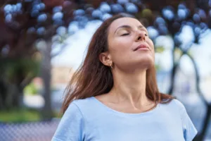 Woman with eyes closed taking a deep breath outdoors, symbolizing clear breathing, respiratory wellness, and natural immune support