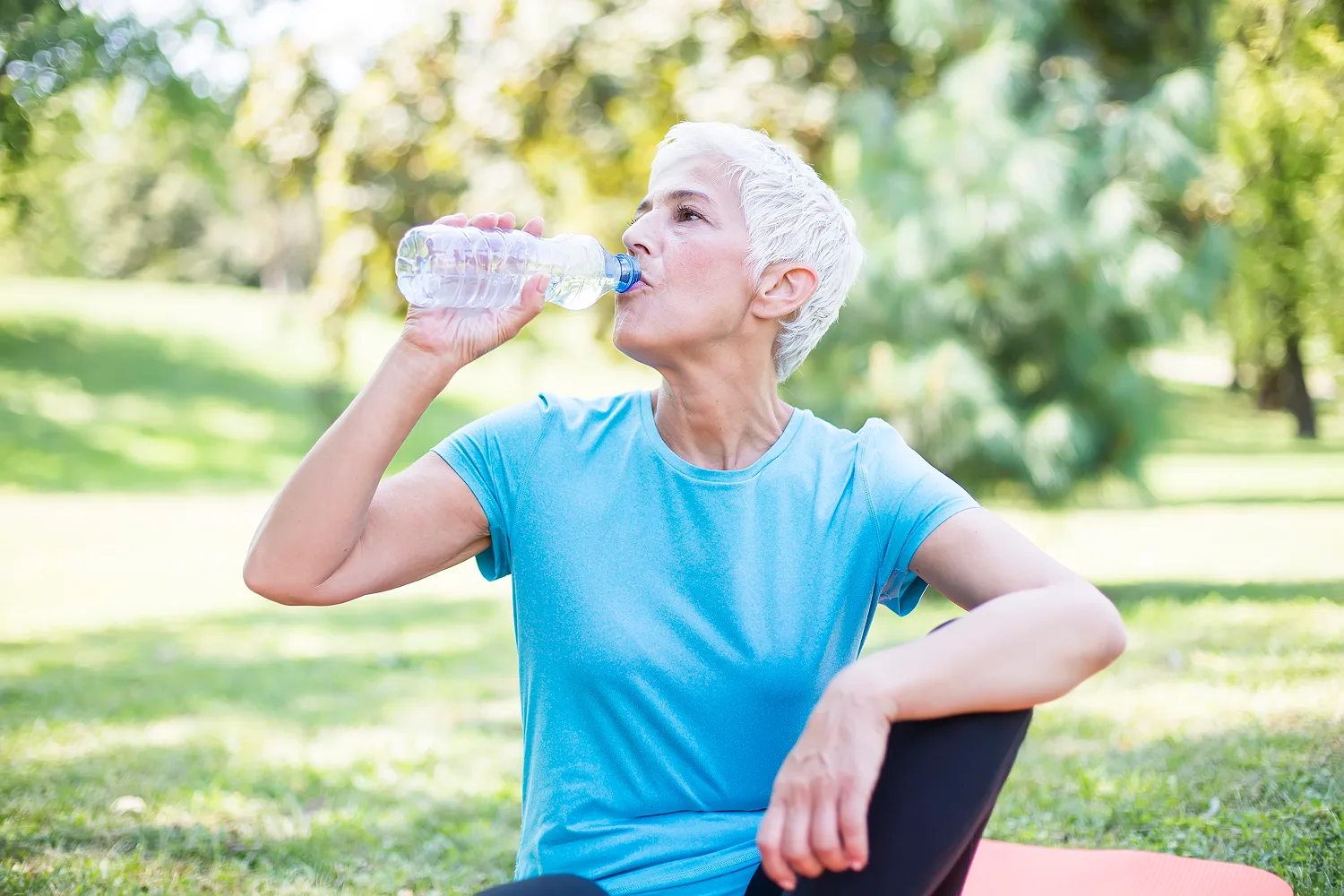 Woman drinking water after exercise outdoors, representing hydration and healthy habits to help reduce menopause hot flashes