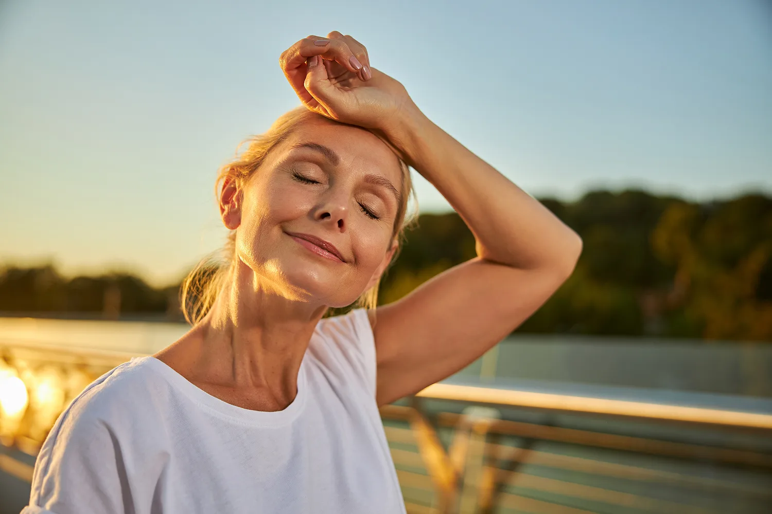 Smiling woman cooling off outdoors at sunset, representing natural relief from hot flashes during menopause