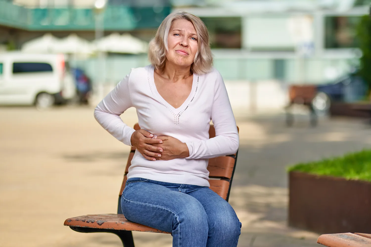 Woman holding her stomach while seated outdoors representing menopause discomfort, hormonal changes, and digestive symptoms.