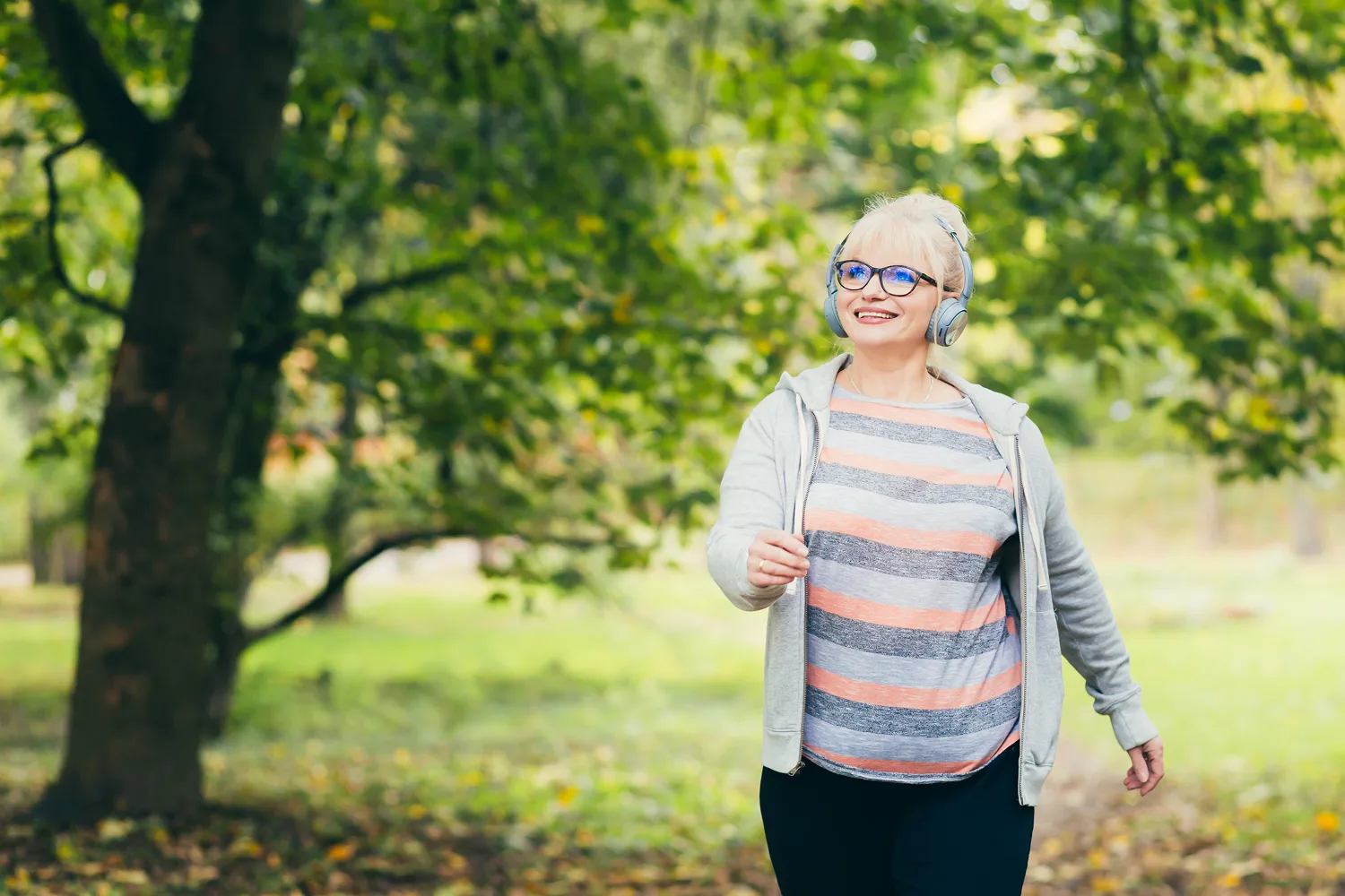 Smiling mature woman walking in nature with headphones representing healthy aging, menopause wellness, and natural lifestyle support.