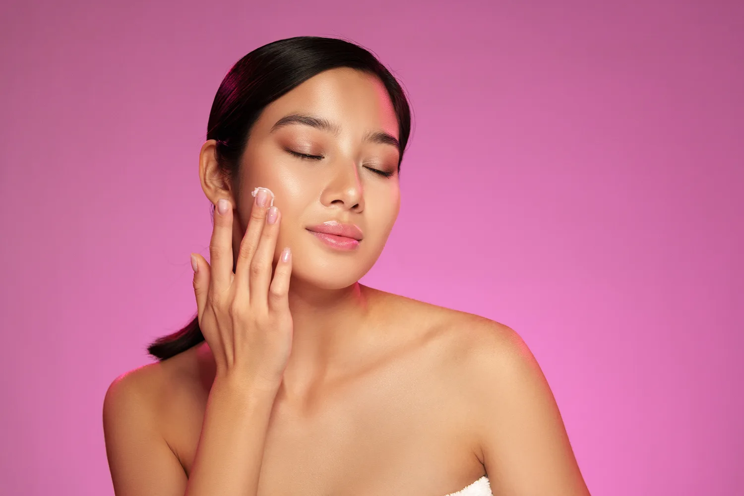 Woman applying moisturizer on glowing skin highlighting benefits of biotin and collagen for skin hydration.