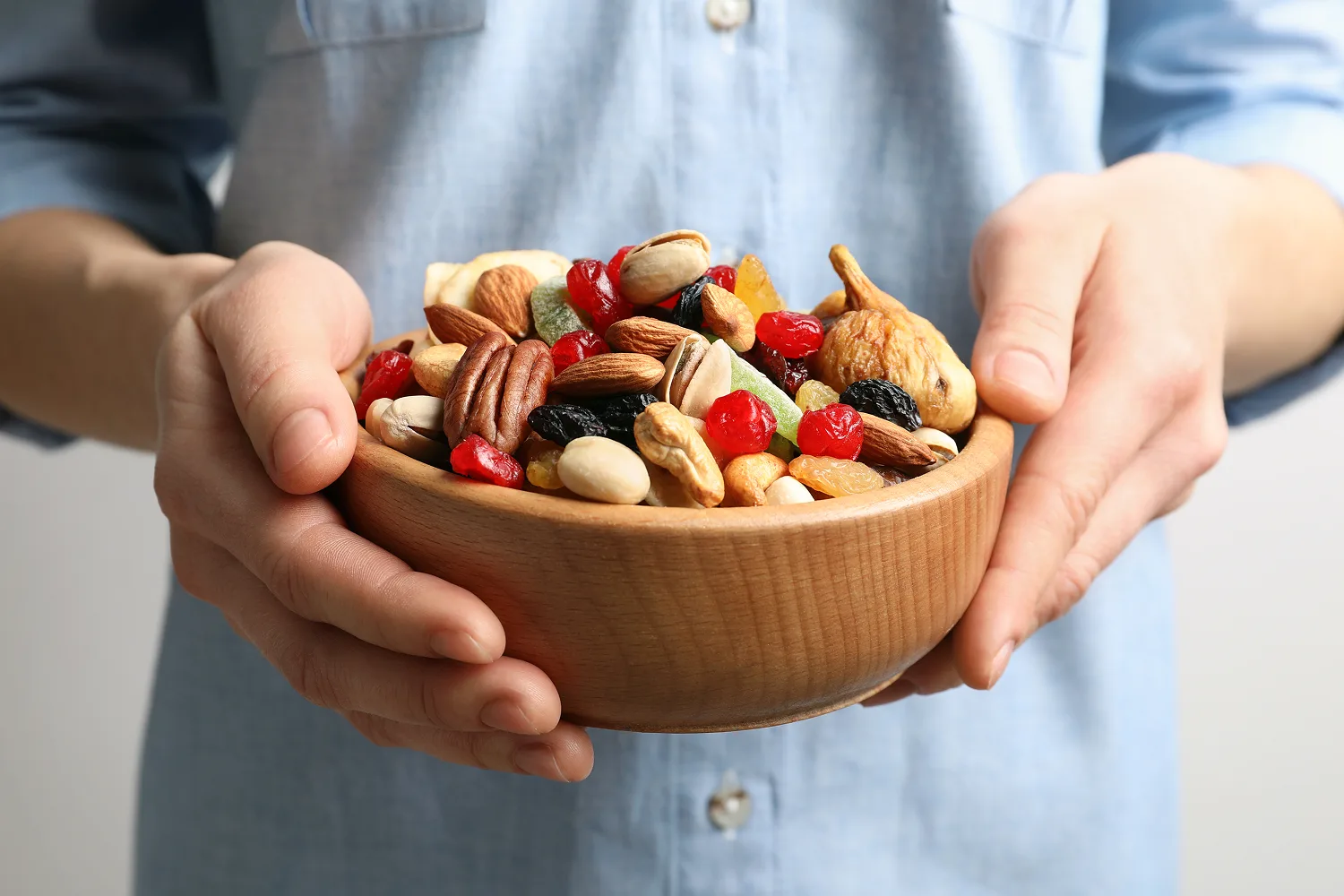 Person holding a bowl of mixed nuts and dried fruits representing healthy snack choices that may still trigger cravings