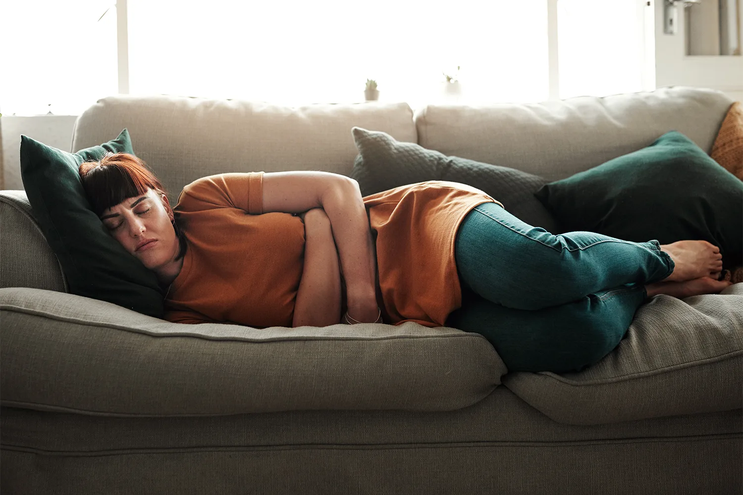 Woman resting on a couch with stomach discomfort showing the effects of stress, fatigue, and lack of proper recovery